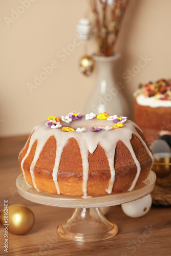Delicious Easter cake decorated with sprinkles near painted eggs on wooden table