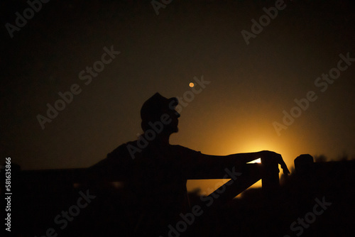 Contraluz de hombre tocando la guitarra bajo un cielo dorado con luna durante el atardecer de la llanura pampeana musico guitarrista pampeano photo