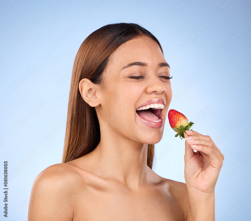 Skincare, health and female with a strawberry in studio with a wellness, natural and face routine. Happy, beauty and woman model eating red fruit for nutrition, diet and self care by blue background. Skincare, health and female with a strawberry in studio with a wellness, natural and face routine. Happy, beauty and woman model eating red fruit for nutrition, diet and self care by blue background.