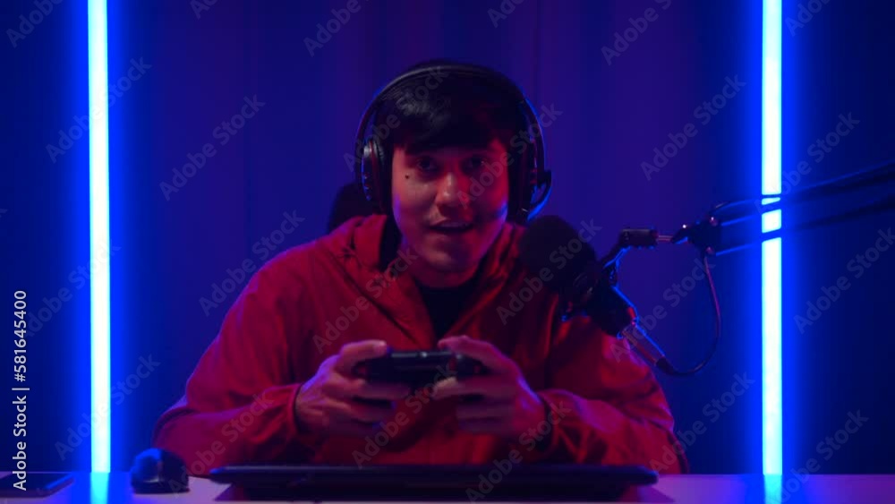 Gamer man playing game and podcast steaming wearing headset with excited feeling at victory moment. Professional Streamer playing game with joystick online in dark room neon light. Gamer man playing game and podcast steaming wearing headset with excited feeling at victory moment. Professional Streamer playing game with joystick online in dark room neon light.