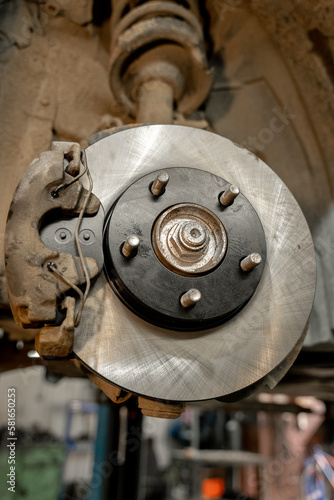 Disc brake on a car, brake disc replacement in a car service. The rim is removed, exposing the rotor and caliper. Close-up.
