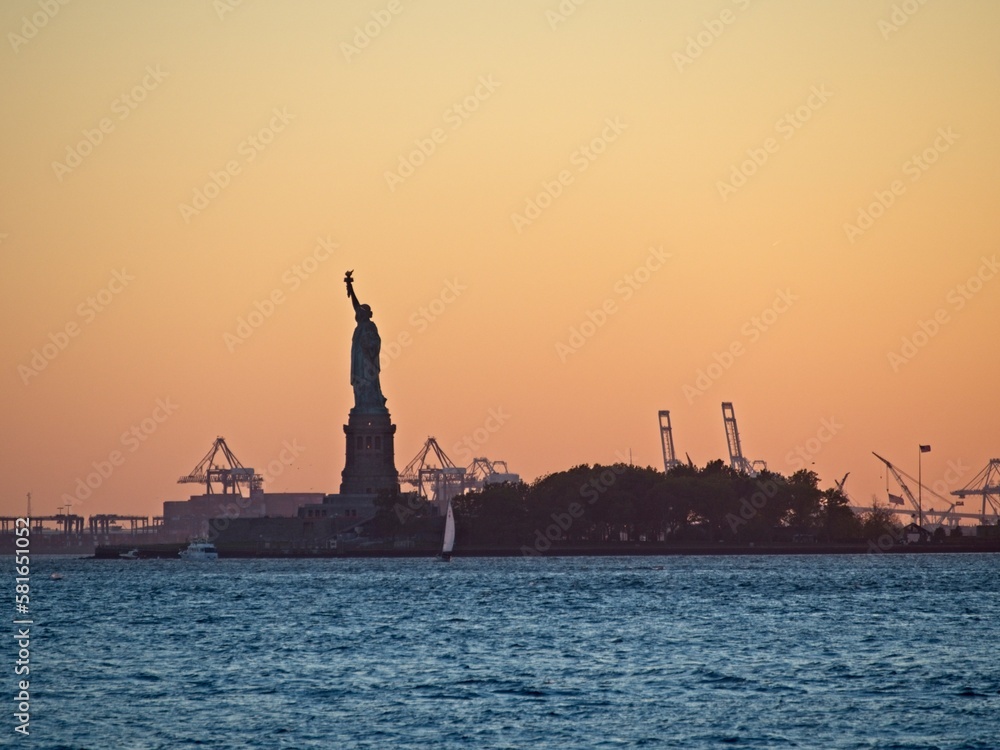 The sun sets over New York City with the Statue of Liberty sitting atop Liberty Island in the New York Harbor