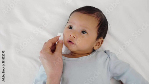mother cleaning and wiping newborn baby face with cotton pad on a bed