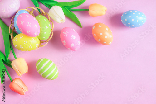 Happy Easter holiday greeting card concept. Colorful Easter Eggs and spring flowers on pastel pink background. Flat lay, top view, copy space.