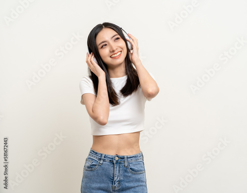 Cheerful asian female teenager listen to the music with white headphone dancing on isolated white background. Beautiful young woman in hand touch a wireless headphone having fun with music.