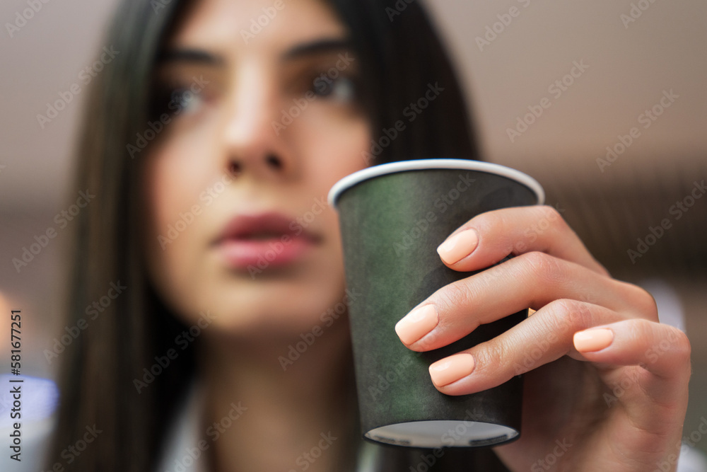 Portrait of a young woman with a cup of coffee.Selective focus on the hand with a cup Portrait of a young woman with a cup of coffee.Selective focus on the hand with a cup