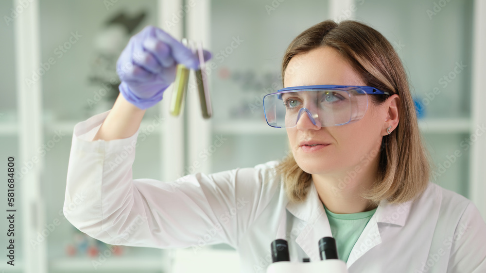 Woman chemist in protective glasses holding test tubes with liquid in hands in laboratory Woman chemist in protective glasses holding test tubes with liquid in hands in laboratory