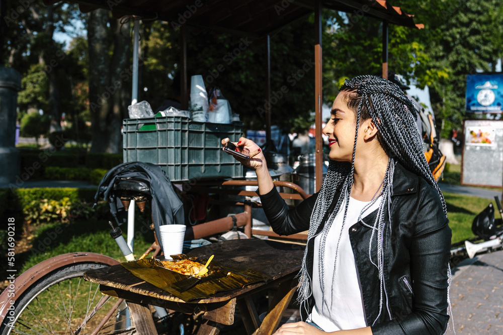 Obraz premium young latin woman with braids hair eating mexican tamales street food on park in Mexico city, hispanic people