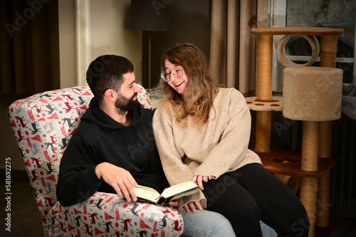 Young couple on a comfortable armchair reading a book together