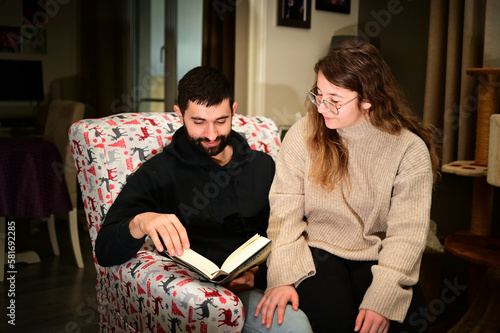Young couple on a comfortable armchair reading a book together