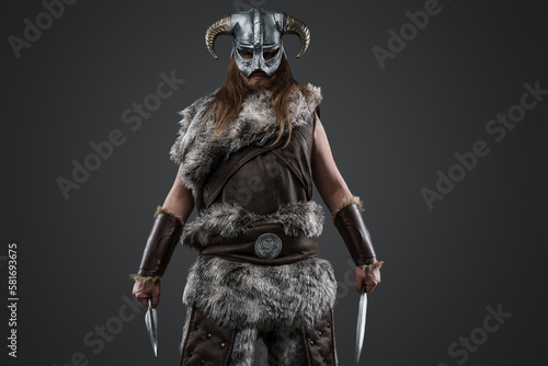 Shot of long haired viking from past with fur and helmet holding two daggers.