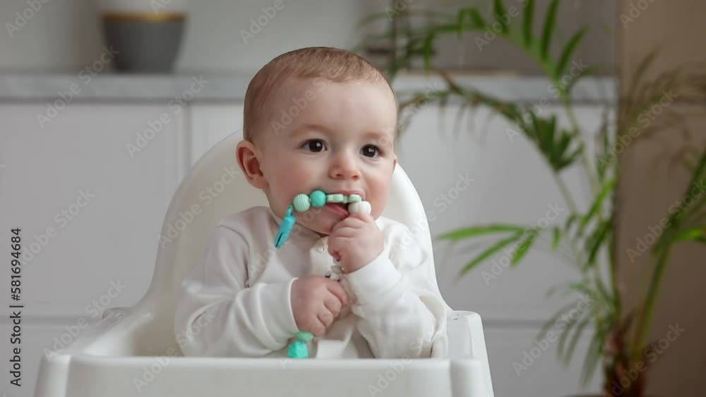 Cute little baby sitting in high chair holding spoon, looking aside smiling, Cute little baby sitting in high chair holding spoon, looking aside smiling,