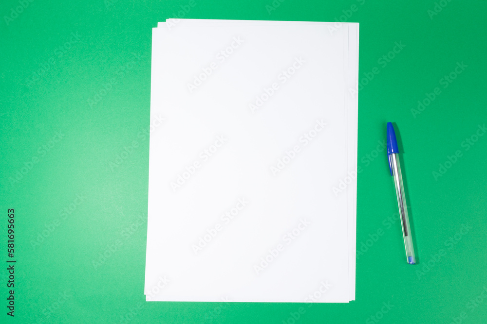 empty white paper sheet and a pen on green background. Mockup empty white paper sheet and a pen on green background. Mockup