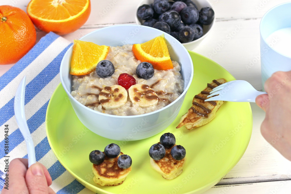 Funny bowls of oatmeal with cat faces, fruits and berries, food idea for kids, top view Funny bowls of oatmeal with cat faces, fruits and berries, food idea for kids, top view