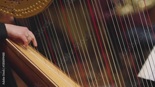 A slow motion video of a musician playing a glissando on a harp during a classical symphony orchestra concert