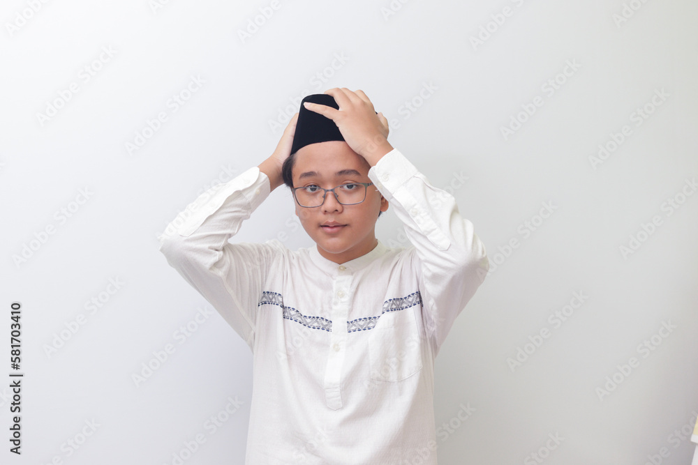 Portrait of young Asian muslim man trying to adjust his songkok or black skullcap. Isolated image on white background
Portrait of young Asian muslim man trying to adjust his songkok or black skullcap. Isolated image on white background
