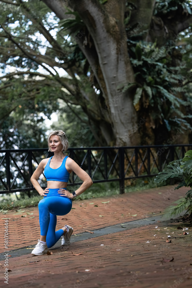 Obraz premium Woman runner stretching legs before run summer park morning Middle age athletic female warming up body before running 