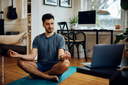 Athletic man follows online Yoga class while using laptop and exercising at home.