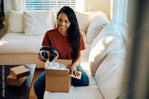 Картината върху платно Happy black woman unpacks new headphones she bought online.