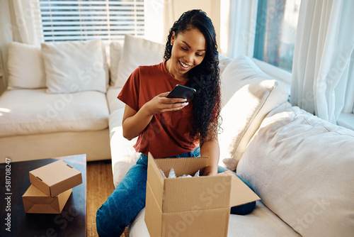 Papier peint Happy black woman using cell phone while unpacking delivery box at home