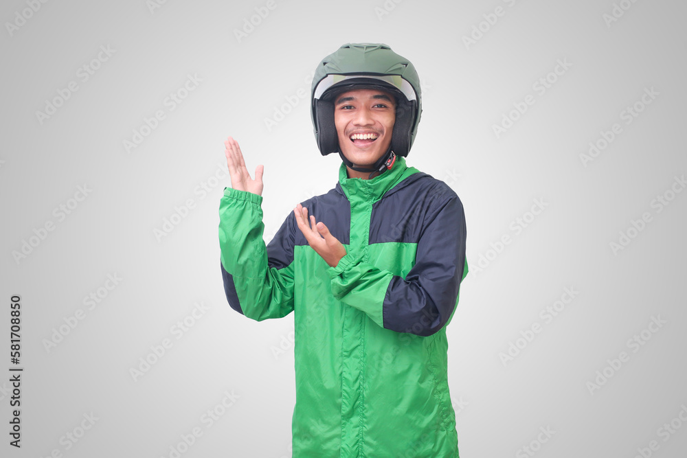 Portrait of Asian online taxi driver wearing green jacket and helmet pointing at empty space with finger. Isolated image on white background Portrait of Asian online taxi driver wearing green jacket and helmet pointing at empty space with finger. Isolated image on white background