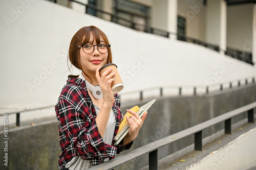 Pretty Asian female college student sipping coffee while walking along the campus building.