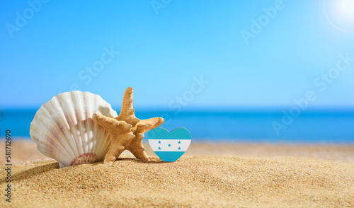 Beautiful beach in the Honduras. Flag of Honduras in the shape of a heart and shells on a sandy beach.