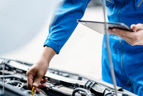 Close up, Auto mechanic repairman using tablet and pulling dipstick to checking engine oil level engine in the engine room, check the mileage of the car, oil change, auto maintenance service concept.