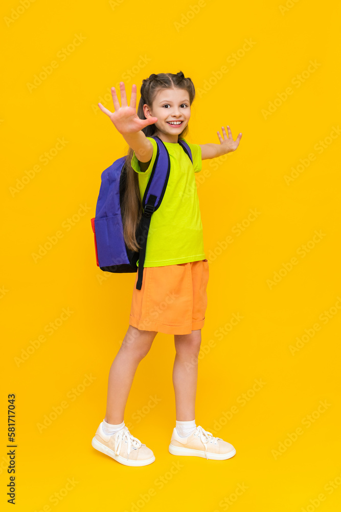 A little girl with a school backpack. A child in summer shorts is going to educational courses. A happy child with a satchel. A full-length schoolgirl on a yellow isolated background. A little girl with a school backpack. A child in summer shorts is going to educational courses. A happy child with a satchel. A full-length schoolgirl on a yellow isolated background.