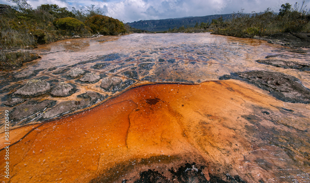 Shallow river with orange and black rock structures on the plateau of