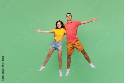 Full body happy excited cool young couple two friends family man woman wear basic t-shirt together jump high with outstretched hands isolated on pastel plain light green background studio portrait.