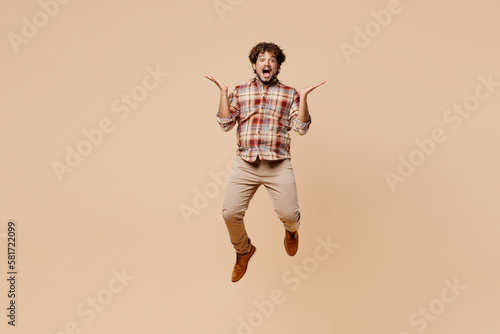 Full body overjoyed young Indian man wears brown shirt casual clothes jump high spread hands say scream wow isolated on plain pastel light beige background studio portrait. People lifestyle concept.