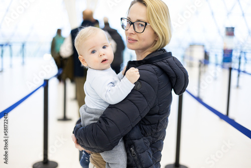 Mother holding his infant baby boy child queuing at airport terminal in passport control line at immigrations departure before moving to boarding gates to board an airplane. Travel with baby concept. photo