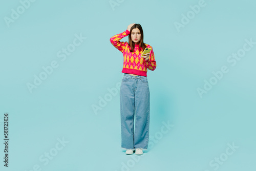 Full body shocked sad displeased young caucasian woman wear bright casual clothes hold head use mobile cell phone isolated on plain pastel light blue cyan background studio portrait Lifestyle concept