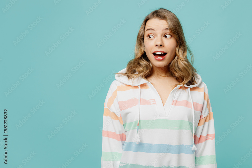 Fototapeta premium Young caucasian surprised shocked excited fun, cool blonde woman wear hoody look aside on workspace area mock up isolated on plain pastel light blue cyan background studio portrait. Lifestyle concept.