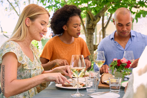 Group Of Friends Enjoying Outdoor Meal And Wine On Visit To Vineyard Restaurant
