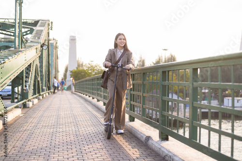 Portrait of young business woman with an electric scooter to work over bridge in modern city  background