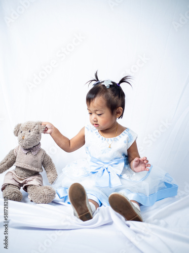 A little 2 year old southeast asian girl sitting down with her teddy bear on white background. 