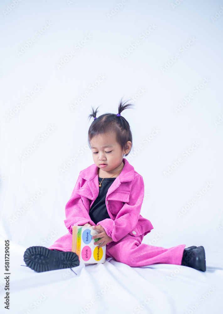 A portrait of a 2 year old girl sitting down, reading colored book on white isolated background. A portrait of a 2 year old girl sitting down, reading colored book on white isolated background.