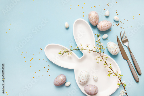 Photography beautiful light easter mockup with bunny plate and cutlery, gold and marble eggs, cherry blossoms and confetti on a pastel blue background