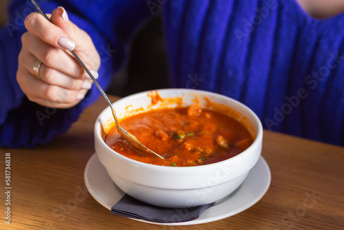 Woman with spoon eating tasty red tomato soup gazpacho with croutons, vegetables and herbs in cafe. Lunch break.