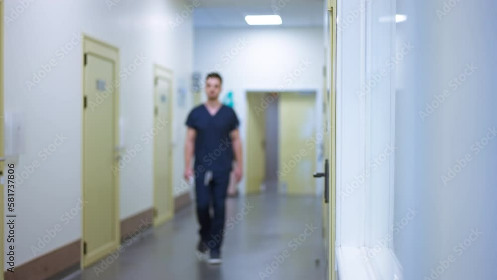 Wide shot hospital corridor with blurred man walking in slow motion passing camera leaving. Serious Middle Eastern confident doctor indoors at workplace Wide shot hospital corridor with blurred man walking in slow motion passing camera leaving. Serious Middle Eastern confident doctor indoors at workplace