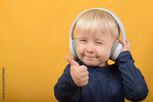 funny boy child listens to music in headphones and shows thumbs up