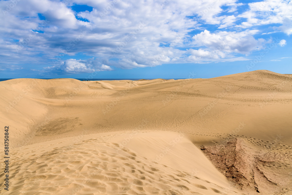View of desert sand dunes against a moody cloudy blue sky. Maspalomas Dunes in Playa del Ingles, Maspalomas, Gran Canaria, Spain.