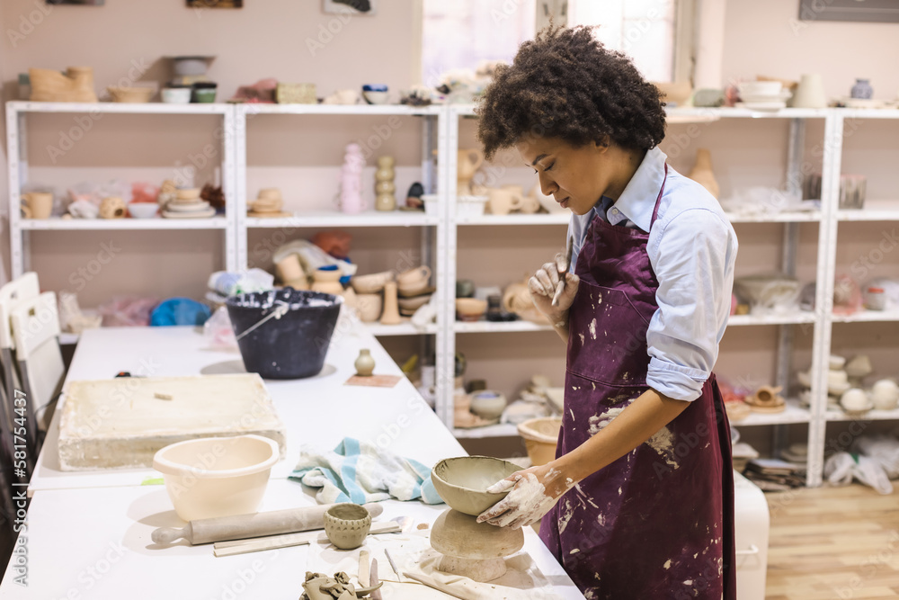 Creativ African American woman proudly stands in her pottery studio, skillfully decorate a clay cup with her hands. Her creative work is the result of years of practice as an artisan potter.