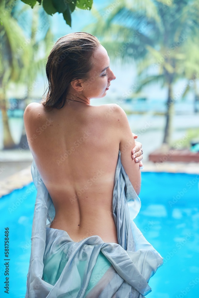 Beautiful young girl by the pool in a tropical place. Summer vacation. Gray clothing covers the body.