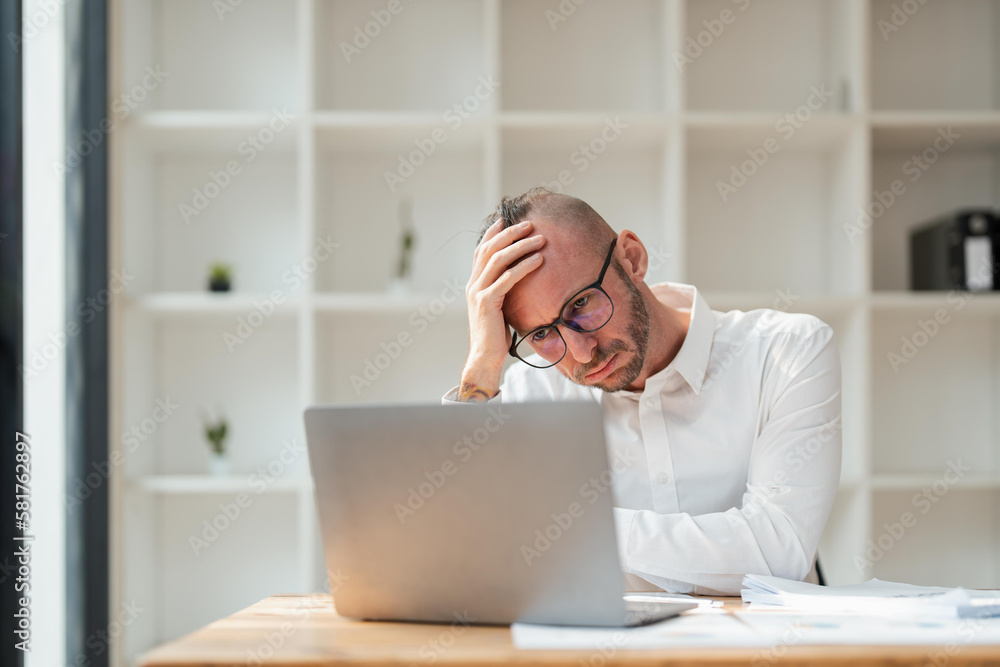 businessmen are worried about the work and the economic downturn. Tired and worried business man at workplace in office holding his head on hands businessmen are worried about the work and the economic downturn. Tired and worried business man at workplace in office holding his head on hands