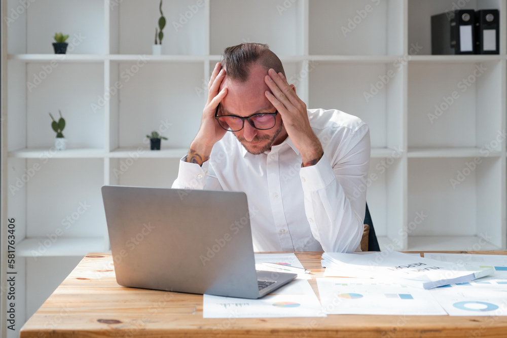 businessmen are worried about the work and the economic downturn. Tired and worried business man at workplace in office holding his head on hands businessmen are worried about the work and the economic downturn. Tired and worried business man at workplace in office holding his head on hands