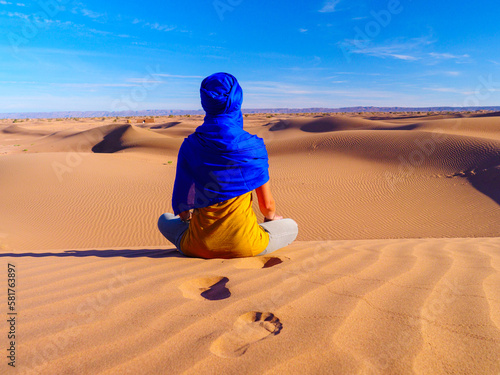 Tableau sur toile Woman with blue berber turban sitting in sahara desert and looking panoramic vie