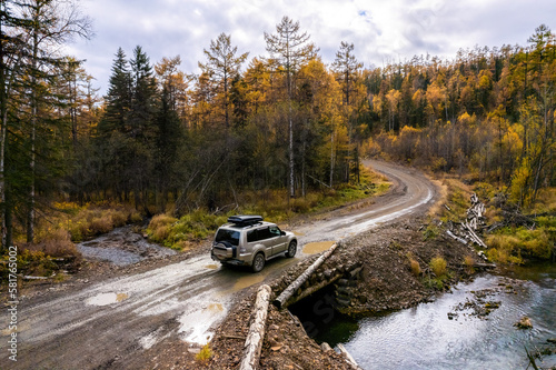 SUV on wooden bridge over small mountain river. Autumn forest.